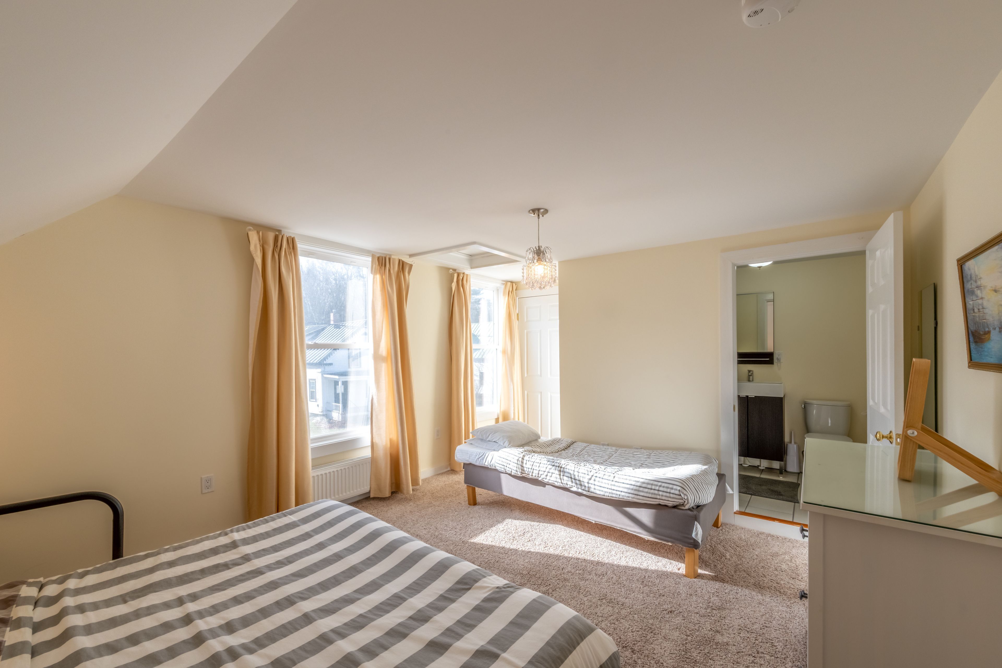 Une chambre avec deux lits, une fenêtre avec des rideaux, un luminaire au plafond et une vue sur l’extérieur.