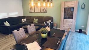 A modern living room with a sectional sofa, a dining table with placemats, and a chandelier with exposed bulbs.