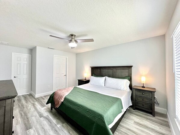 Un dormitorio con cama, mesitas de noche, ventilador de techo y cómoda.