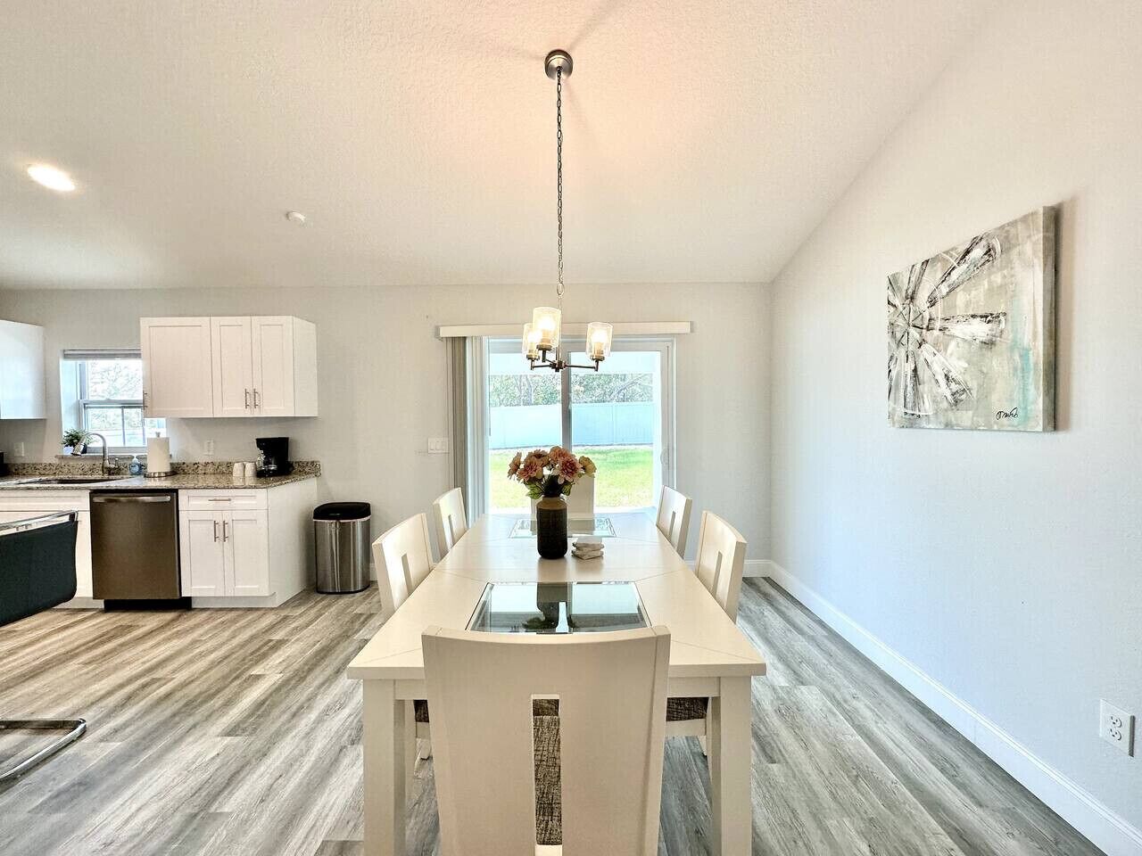 Une cuisine moderne avec des meubles blancs, une table à manger avec des chaises et un lustre.