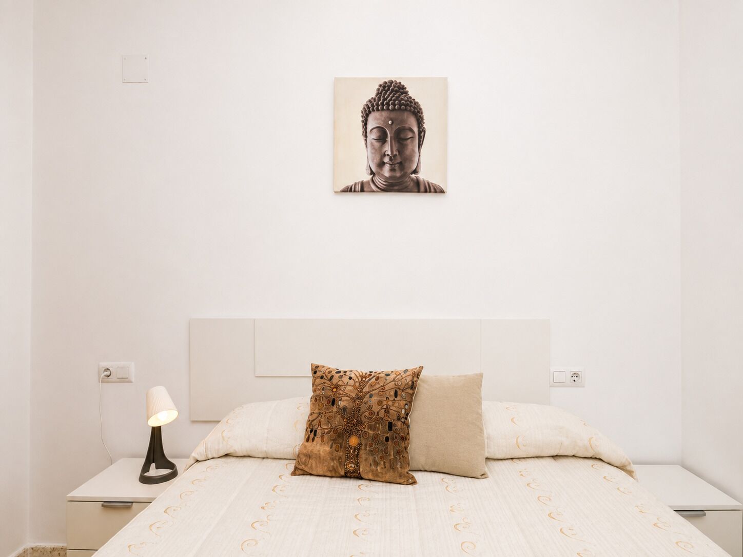 Une chambre à coucher au style minimaliste, avec un lit, un coussin décoratif, un tableau accroché au mur et une lampe de chevet.