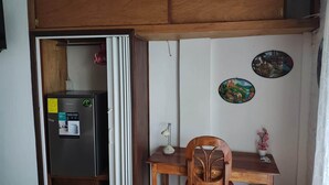 A compact kitchen with a refrigerator, a wooden table, and two wall decorations. - Lombardia Planes de Renderos - Casa de Piedra (San Salvador)