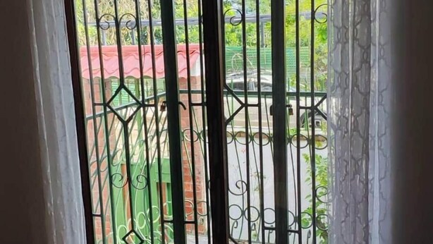 A room with a bed, a sliding glass door with a metal gate, and a view of a green outdoor area. - Lombardia Planes de Renderos - Casa de Piedra (San Salvador)