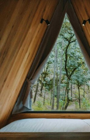 A wooden tent-like structure with a window, a white mattress, and a forest view. - Glamping Uno (Valle de Bravo)