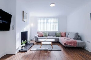 Een moderne woonkamer met een bank, een salontafel, een televisie en een raam met zonwering.