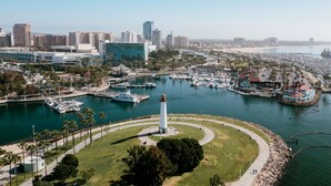 Un puerto deportivo con barcos, un faro y el perfil urbano de una ciudad al fondo.