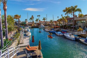 A marina with boats docked, a wooden dock with lounge chairs, and palm trees. - Beach Getaway: 1BR Apt w/ Kitchen & Garage Parking (Long Beach)