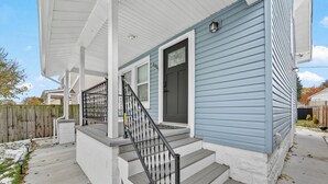 Ein zweistöckiges Haus mit überdachter Veranda, einer Haustür und einer Treppe, die zum Eingang führt.