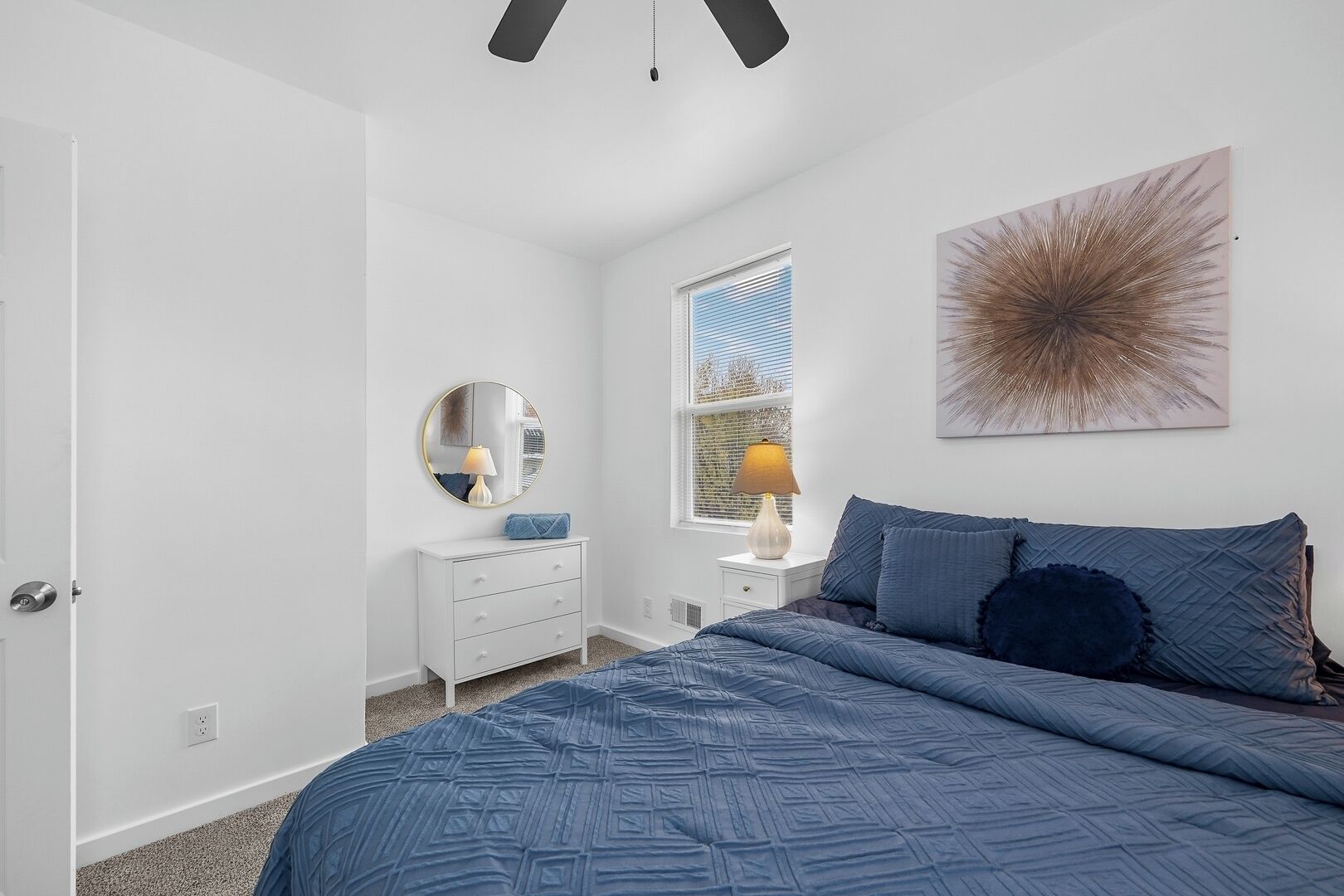 A bedroom with a bed, a dresser, a mirror, and a window with blinds.