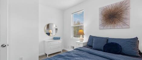 A bedroom with a bed, a dresser, a mirror, and a window with blinds.