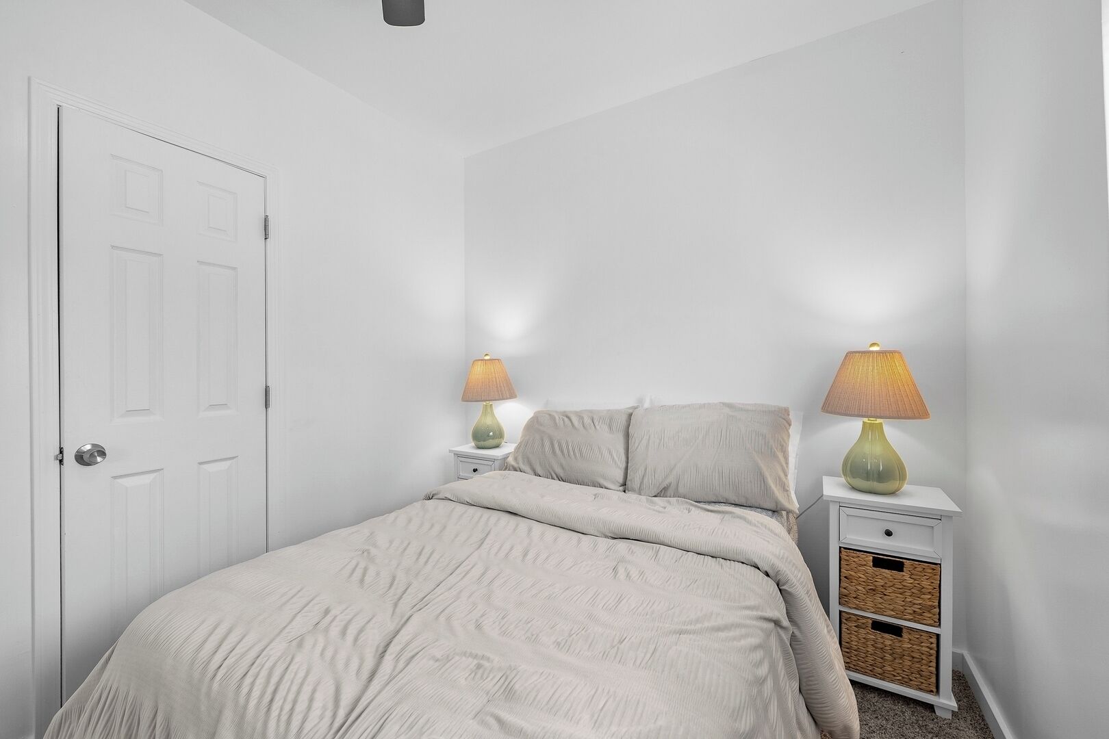 Ein Schlafzimmer mit einem Bett, zwei Nachttischen mit Lampen, einer weißen Tür und einer weißen Wand.