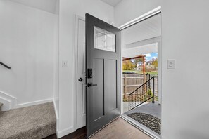 A modern entryway with a dark door, a small window, and a view of a backyard with a wooden fence and a covered patio. - Stylish Family Retreat 10 Guests & Parking (Detroit)