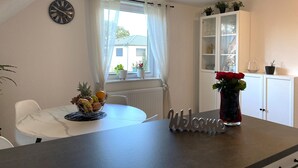 A dining area with a table, chairs, a fruit basket, a vase with flowers, a clock, and a cabinet with glassware. - Modern feel-good apartment in the Illertal (Dettingen an der Iller)