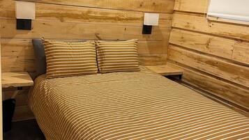 Ein Zimmer mit einer Holzvertäfelung, einem Bett mit gestreifter Bettwäsche, zwei Nachttischlampen und einem Fenster mit Jalousie.