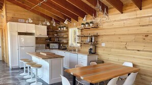 A modern kitchen with white cabinets, a central island with stools, and pendant lighting. - Chalet L'Orée Étoilée (La Bostonnais)