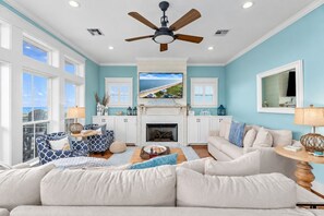 A living room with a fireplace, a ceiling fan, and a large window overlooking the ocean. - Beachfront | 4BR | Sleeps 14 | Pet-Friendly | NEW Hot Tub (Galveston)