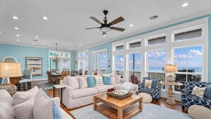 A spacious living room with a large window overlooking the ocean, a ceiling fan, and a dining area with a view. - Beachfront | 4BR | Sleeps 14 | Pet-Friendly | NEW Hot Tub (Galveston)