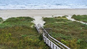 A wooden boardwalk leading to a beach with grassy dunes and the ocean in the background. - Beachfront | 4BR | Sleeps 14 | Pet-Friendly | NEW Hot Tub (Galveston)