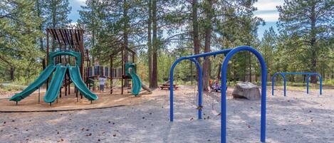 A playground with slides and swings, surrounded by trees.