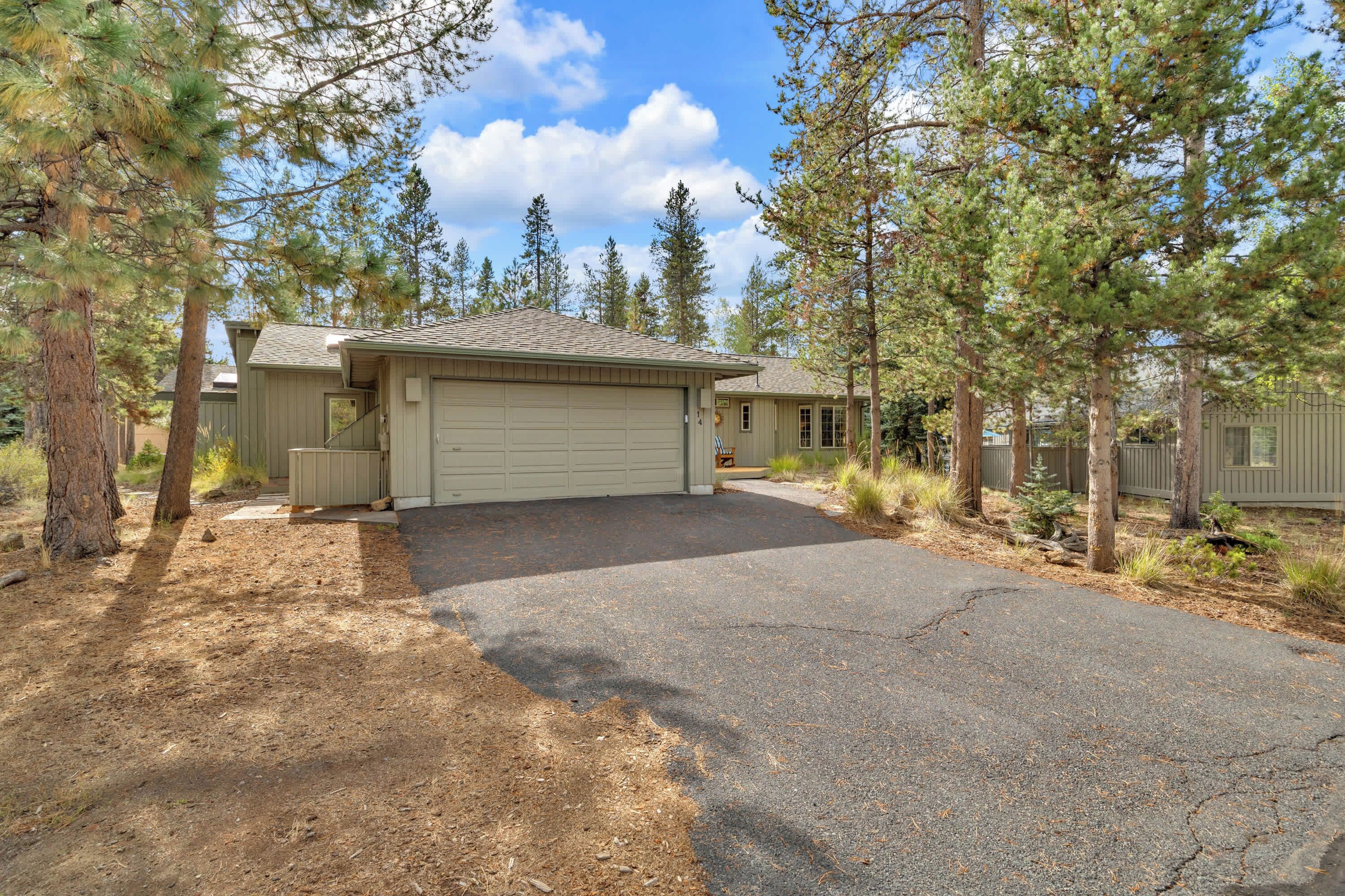 A two-story house with a garage, surrounded by tall pine trees.