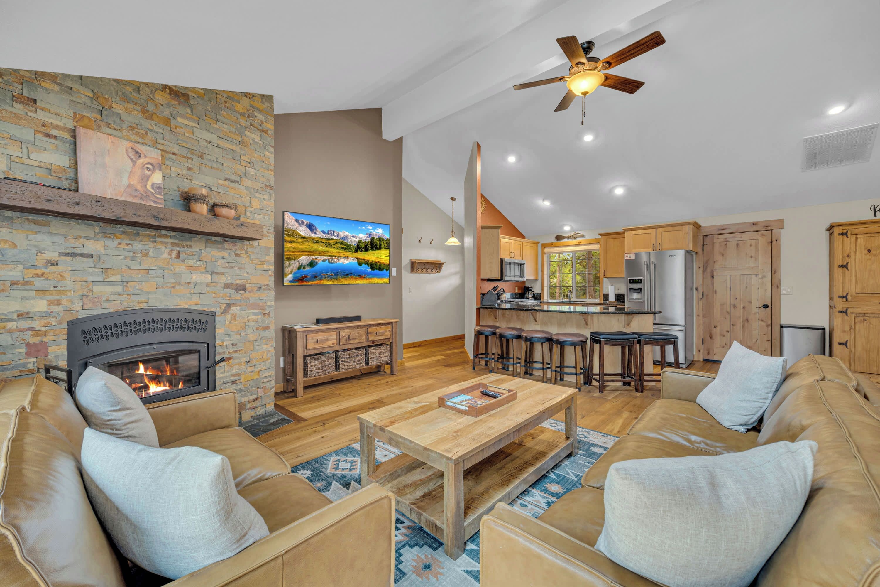 A spacious living room with a fireplace, a dining area with bar stools, and a kitchen with wooden cabinets.