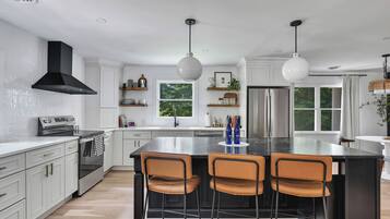 Una cocina moderna con armarios blancos, una isla grande con taburetes de bar, electrodomésticos de acero inoxidable e iluminación colgante.