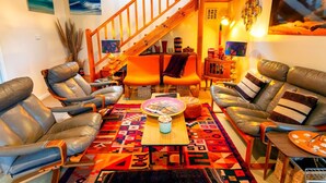 A cozy living room with leather sofas, a colorful rug, and a wooden staircase. - Retro Dunes - Wi-Fi. Linens. Fireplace. Pets OK (Venus Bay)