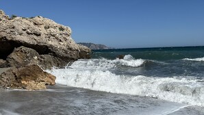Ein Strand mit brechenden Wellen, felsigen Klippen und wolkenlosem, blauem Himmel.