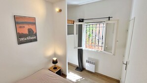 Et soveværelse med en seng, et natbord med lampe, et vindue med udsigt til grønne omgivelser, og et plakat på væggen.
