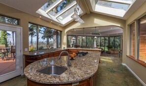 A kitchen with skylights, granite island, and an opening to an adjoining sunroom. - Rustic Retreat with Bay Views (Bayside)