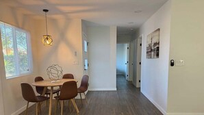 Un comedor con una mesa y sillas de madera, una lámpara colgante y vistas a un pasillo.