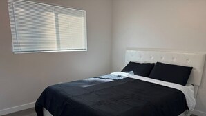 Un dormitorio con una cama, cabecera blanca y una ventana con persianas.