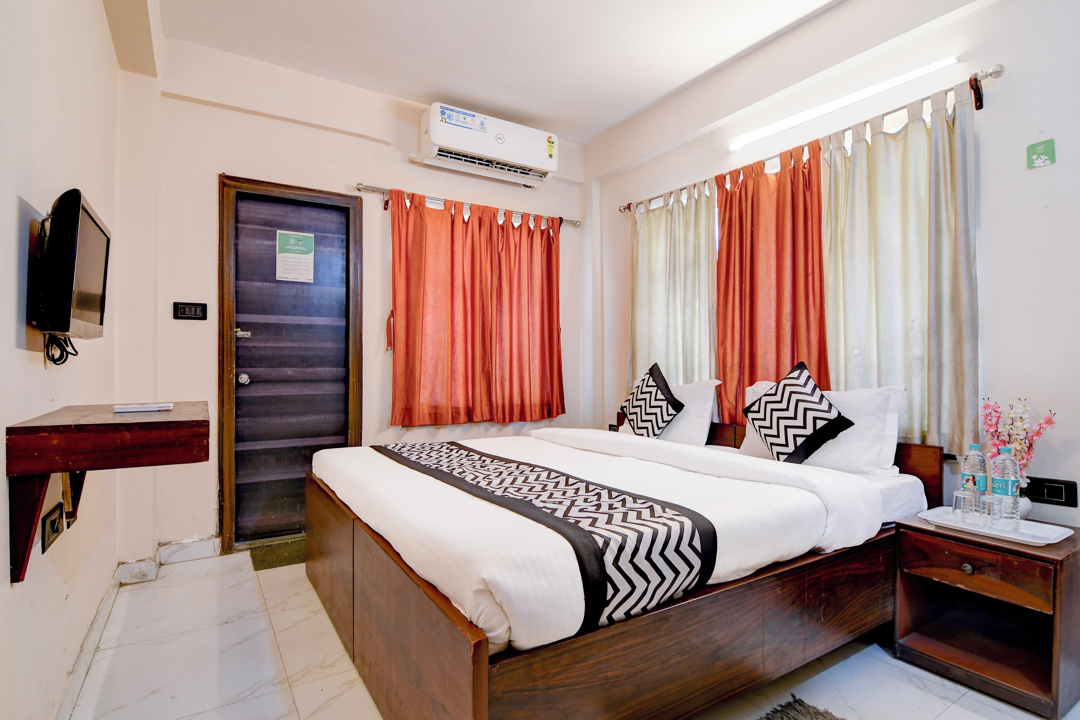 A hotel room with a wooden bed, a bedside table with a tray, a TV, and curtains.