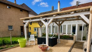 A covered patio area with a seating arrangement, a raised garden bed, and a view of a yellow building.