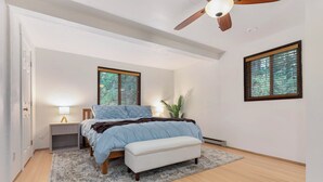 Un dormitorio con cama, mesitas de noche, ventilador de techo y ventanas con persianas.