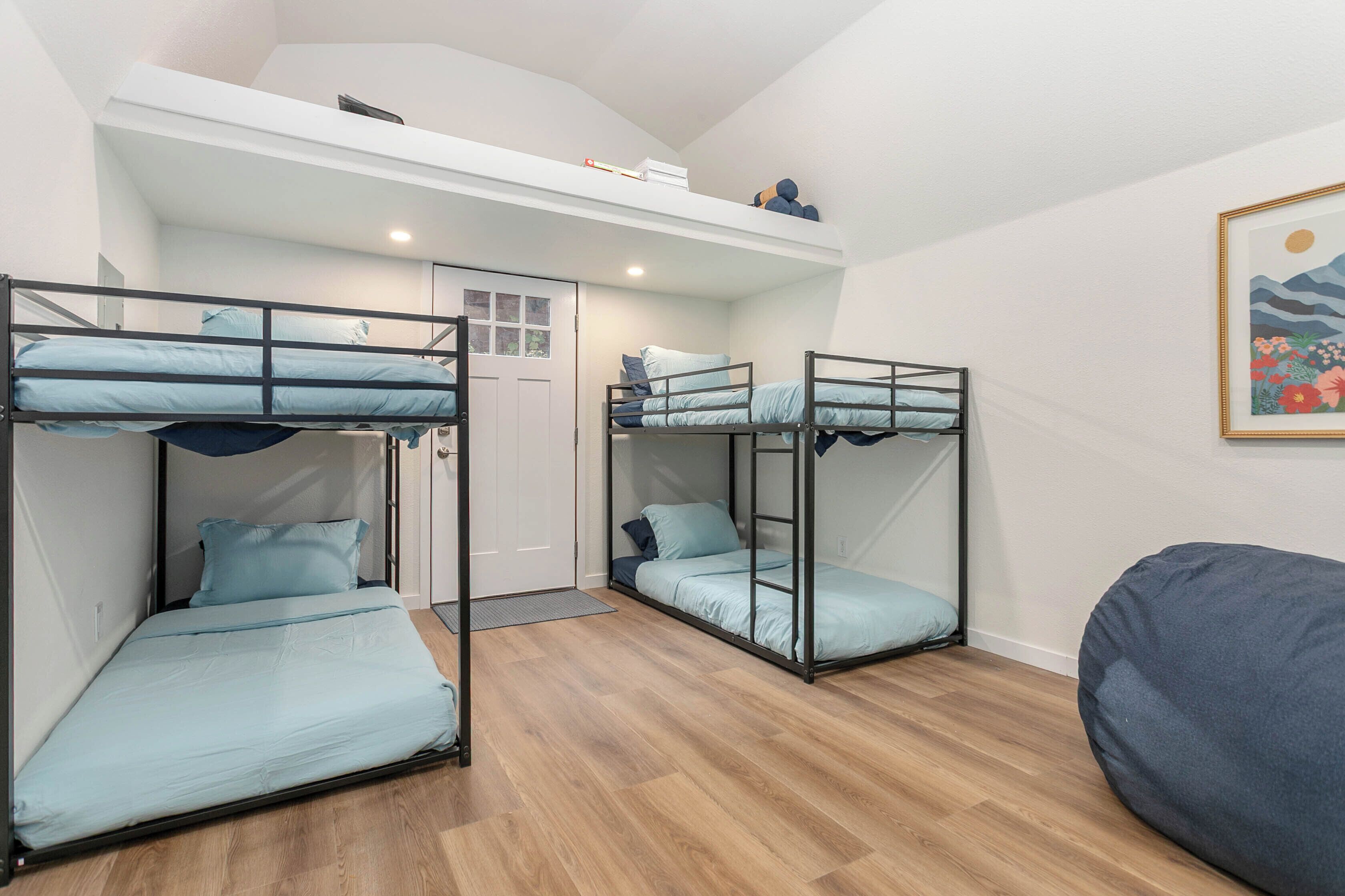 A dormitory room with bunk beds, a door, a small desk, and a framed picture on the wall.