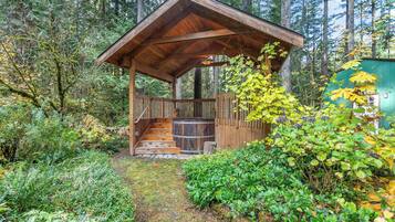 A wooden cabin with a porch and stairs leading up to it, surrounded by dense forest.