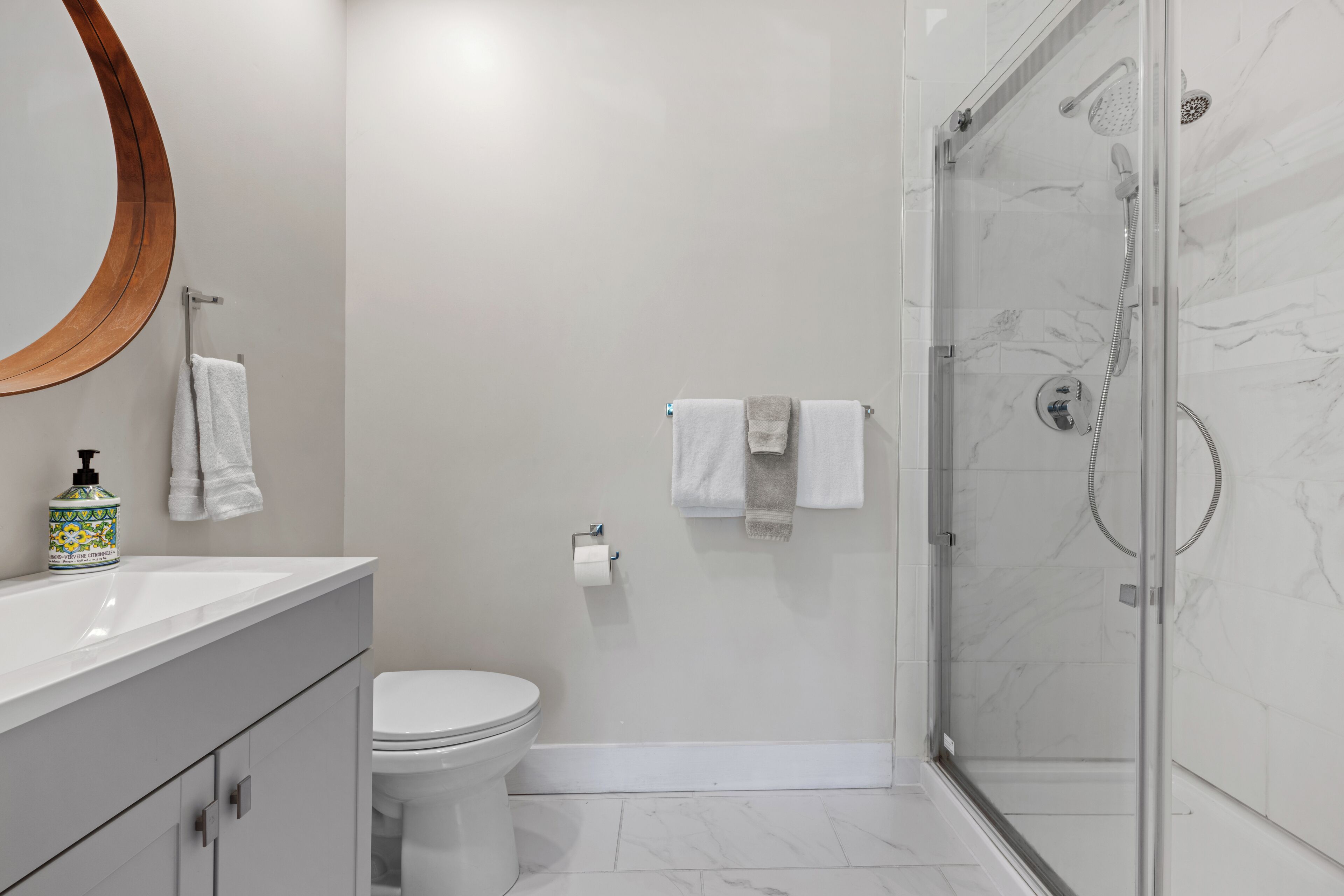 A modern bathroom with a toilet, a sink with a soap dispenser, a mirror, and a glass-enclosed shower area.