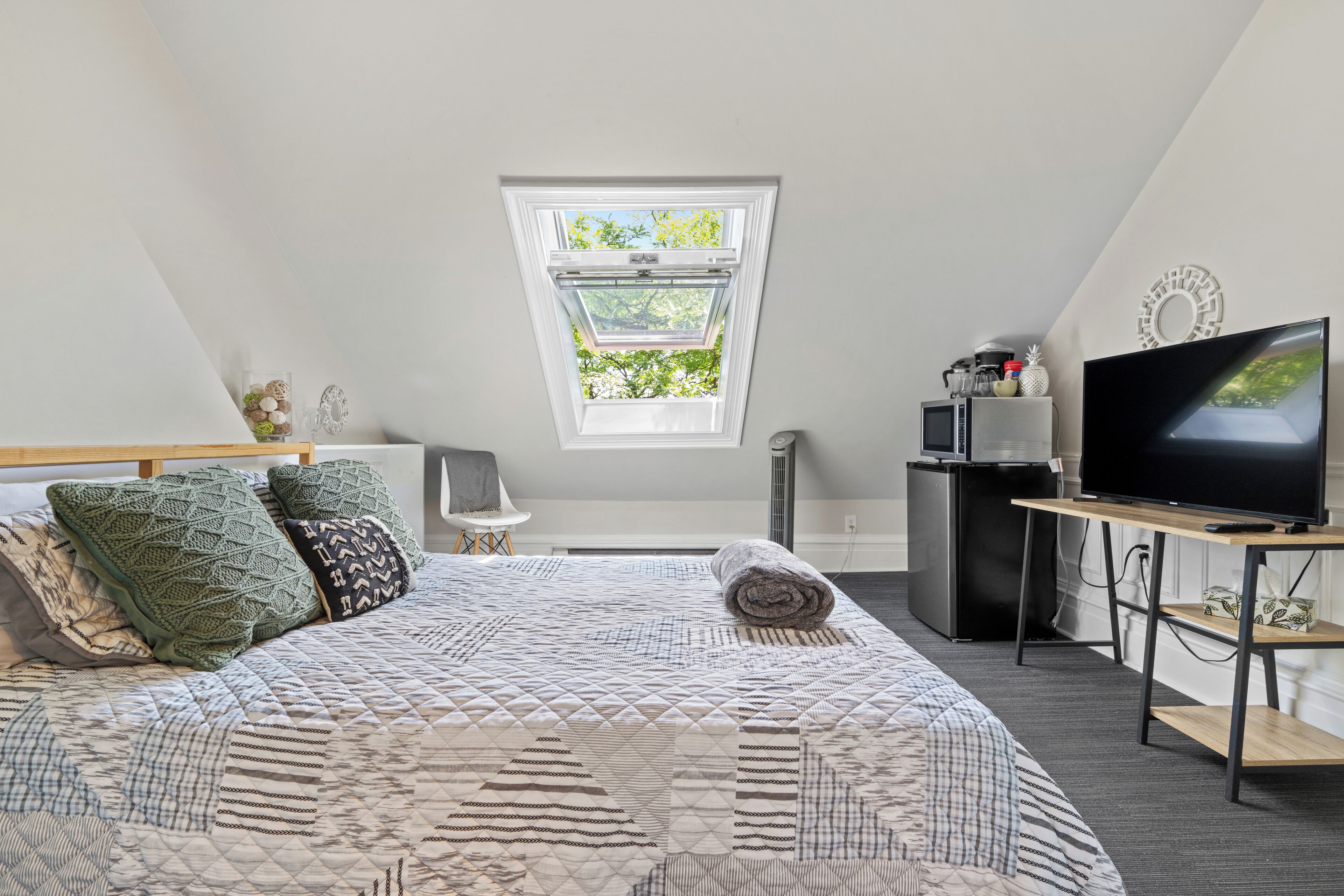 Ein Schlafzimmer mit einem großen Bett, einem Fernseher, einem kleinen Schreibtisch, einem Fenster und einem Deckenventilator.