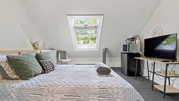 Ein Schlafzimmer mit einem großen Bett, einem Fernseher, einem kleinen Schreibtisch, einem Fenster und einem Deckenventilator.