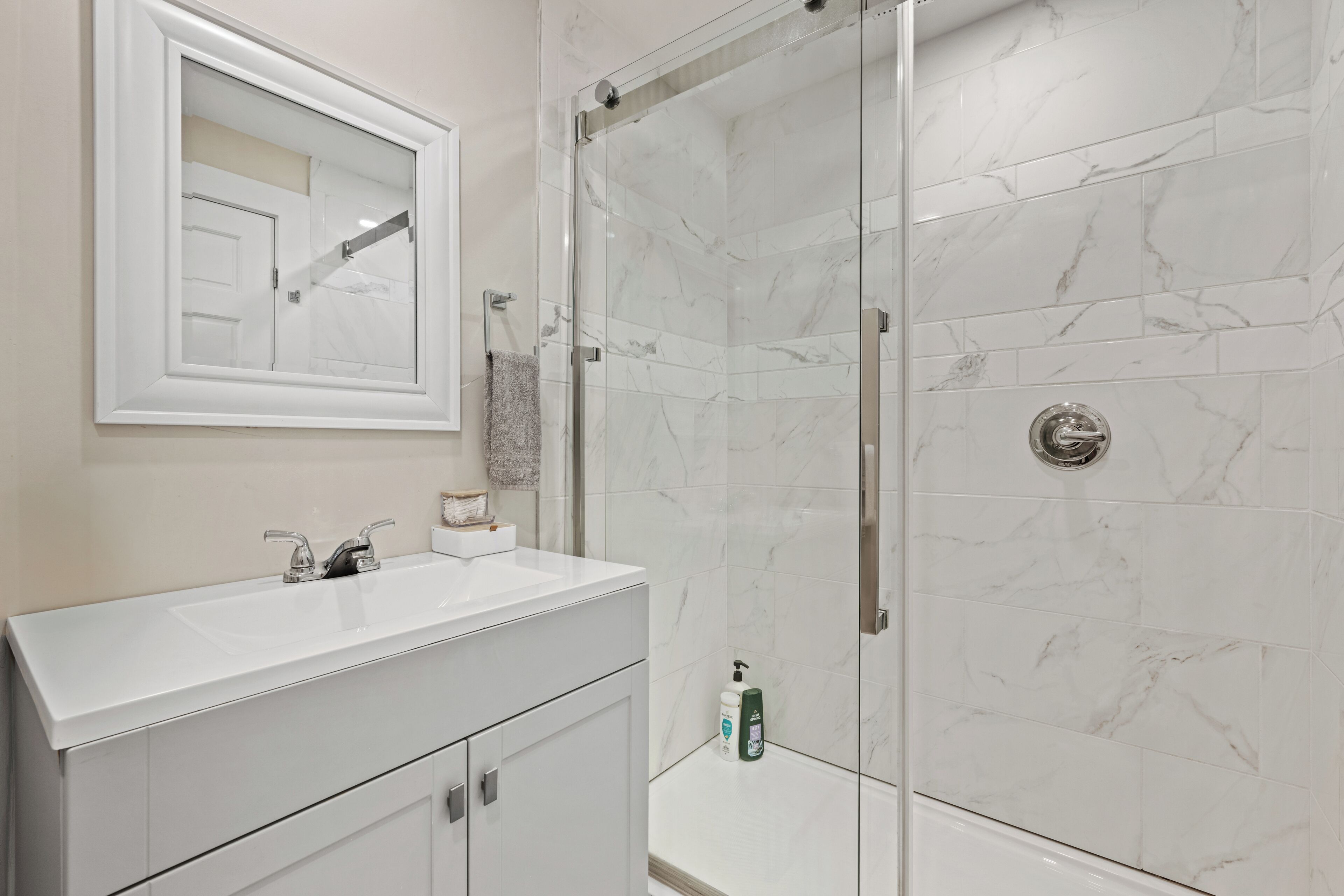 A modern bathroom with a white vanity, a glass shower enclosure, and marble tiles.