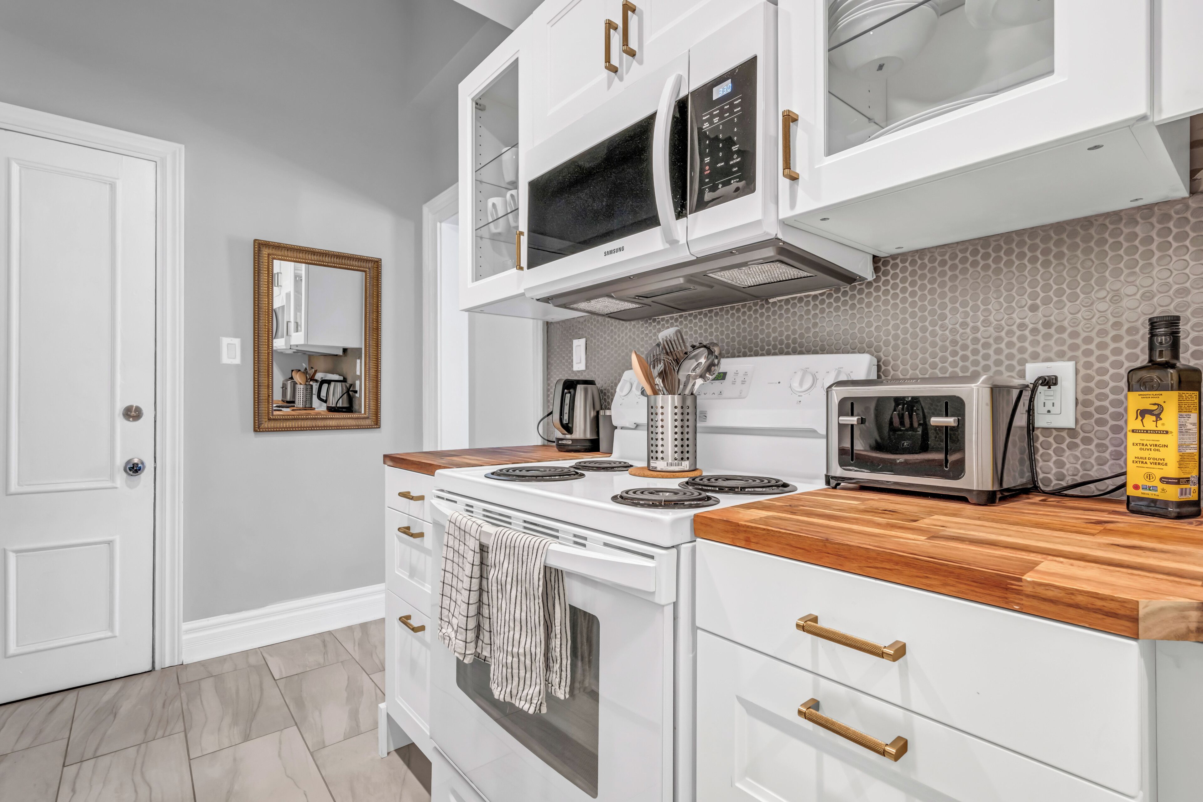 A kitchen with white cabinets, a microwave, a stove, and a wooden countertop.