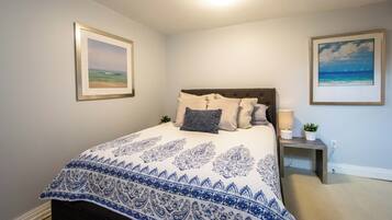 A bedroom with a bed, pillows, a bedside table with a lamp, and two framed pictures on the wall.