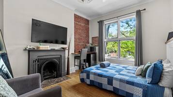 A bedroom with a fireplace, a bed with a blue quilt, a desk, and a TV on the wall.