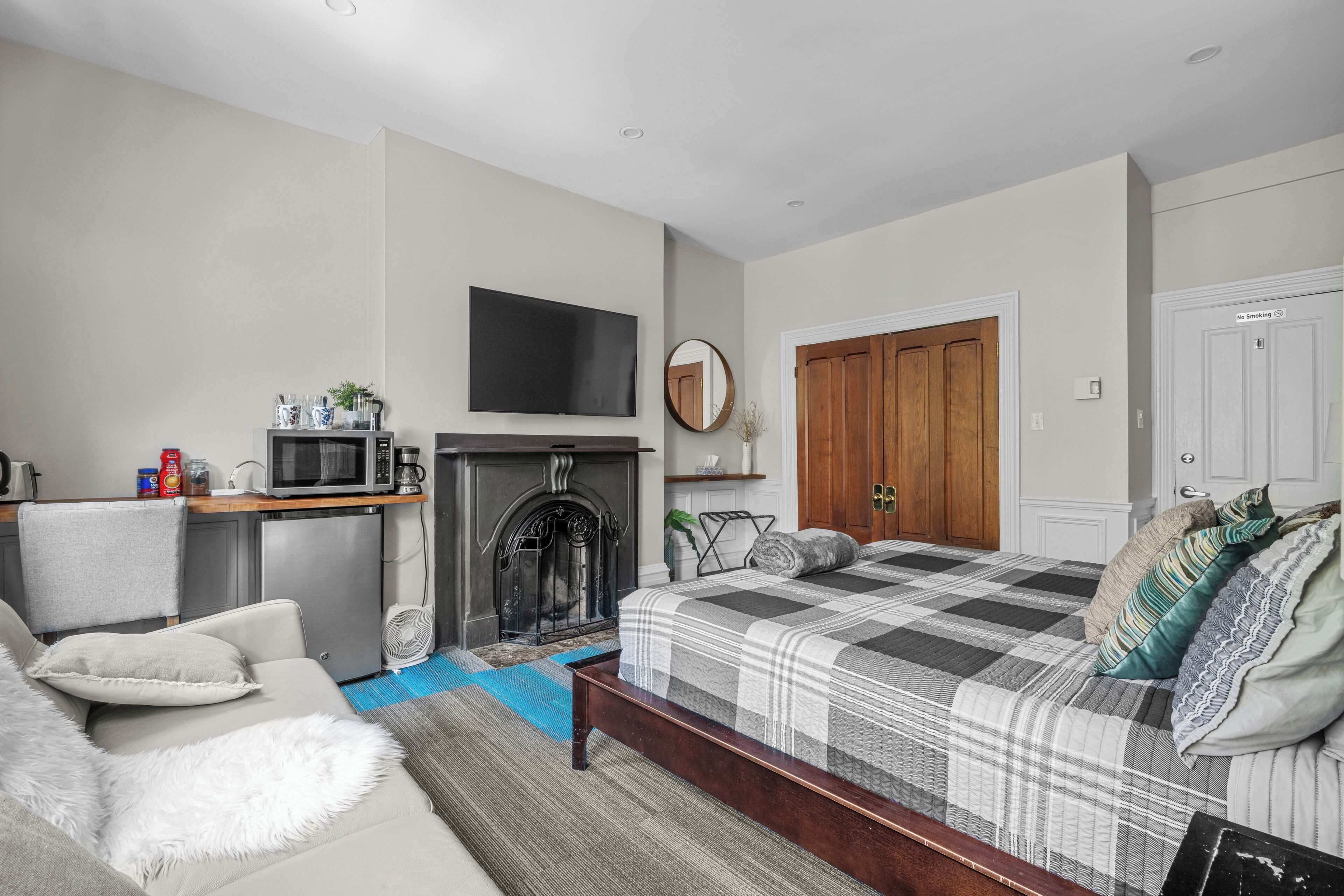 A bedroom with a bed, a sofa, a fireplace, a television, and a wardrobe.