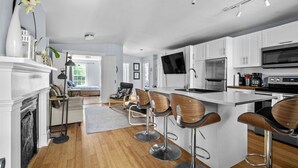 A modern kitchen with white cabinets, a large island with bar stools, a flat-screen TV, and stainless steel appliances. - Red George Inn and Suites (Halifax)