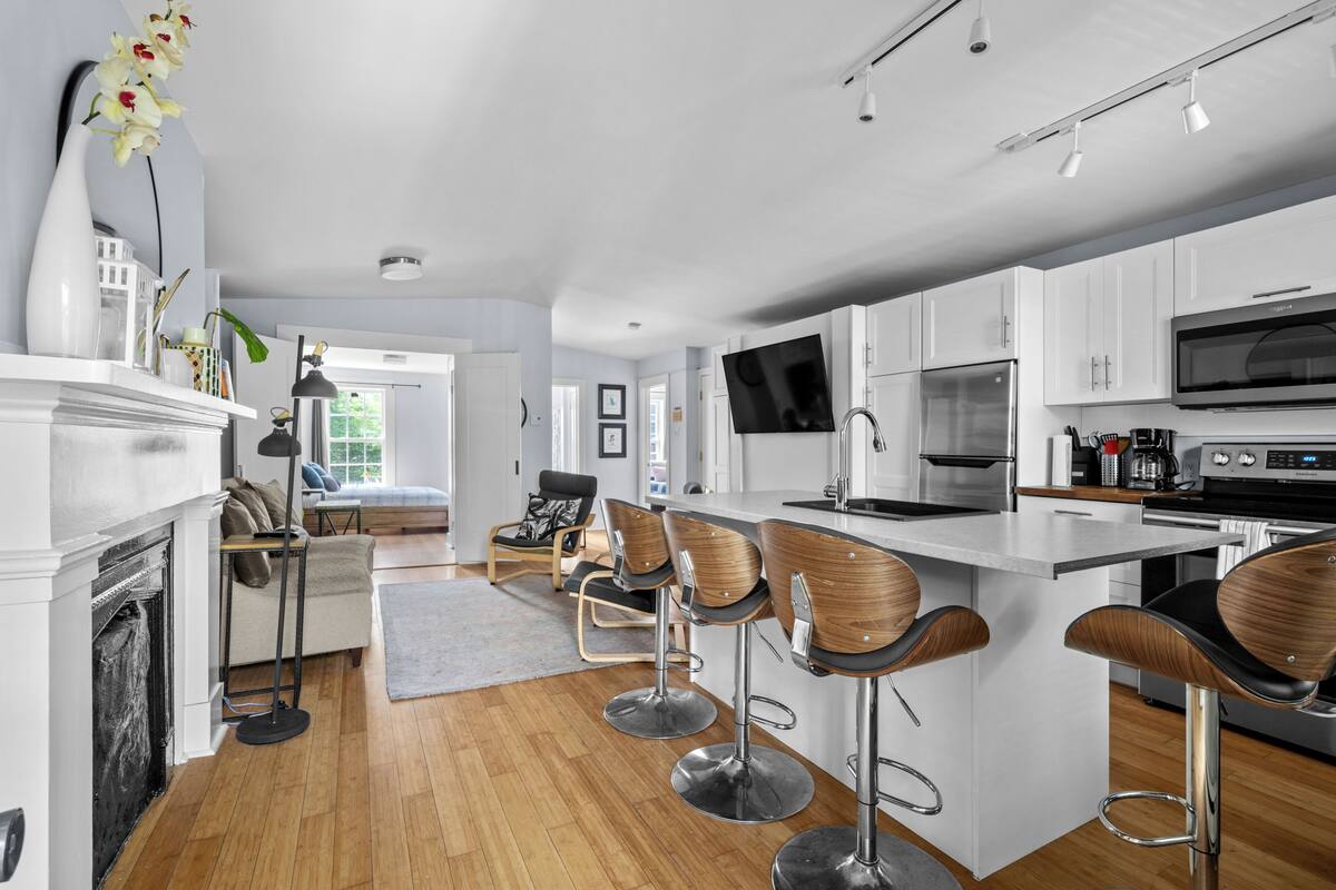 A modern kitchen with white cabinets, a large island with bar stools, a flat-screen TV, and stainless steel appliances.