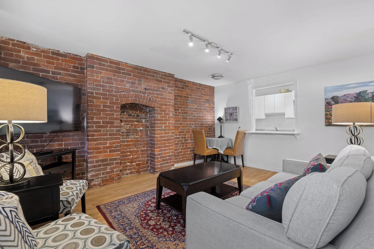 A living room with a brick wall, a flat-screen TV, a coffee table, a sofa, and a patterned rug.
