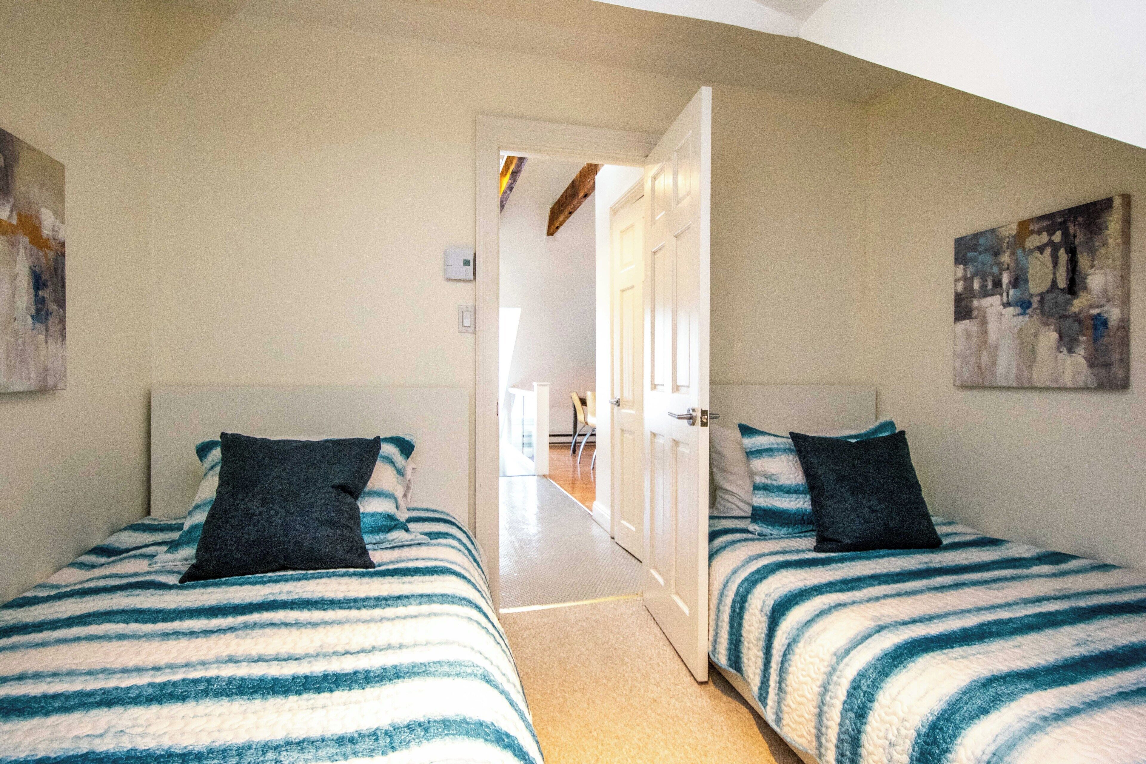 A room with two beds, a door leading to a hallway, and a painting on the wall.