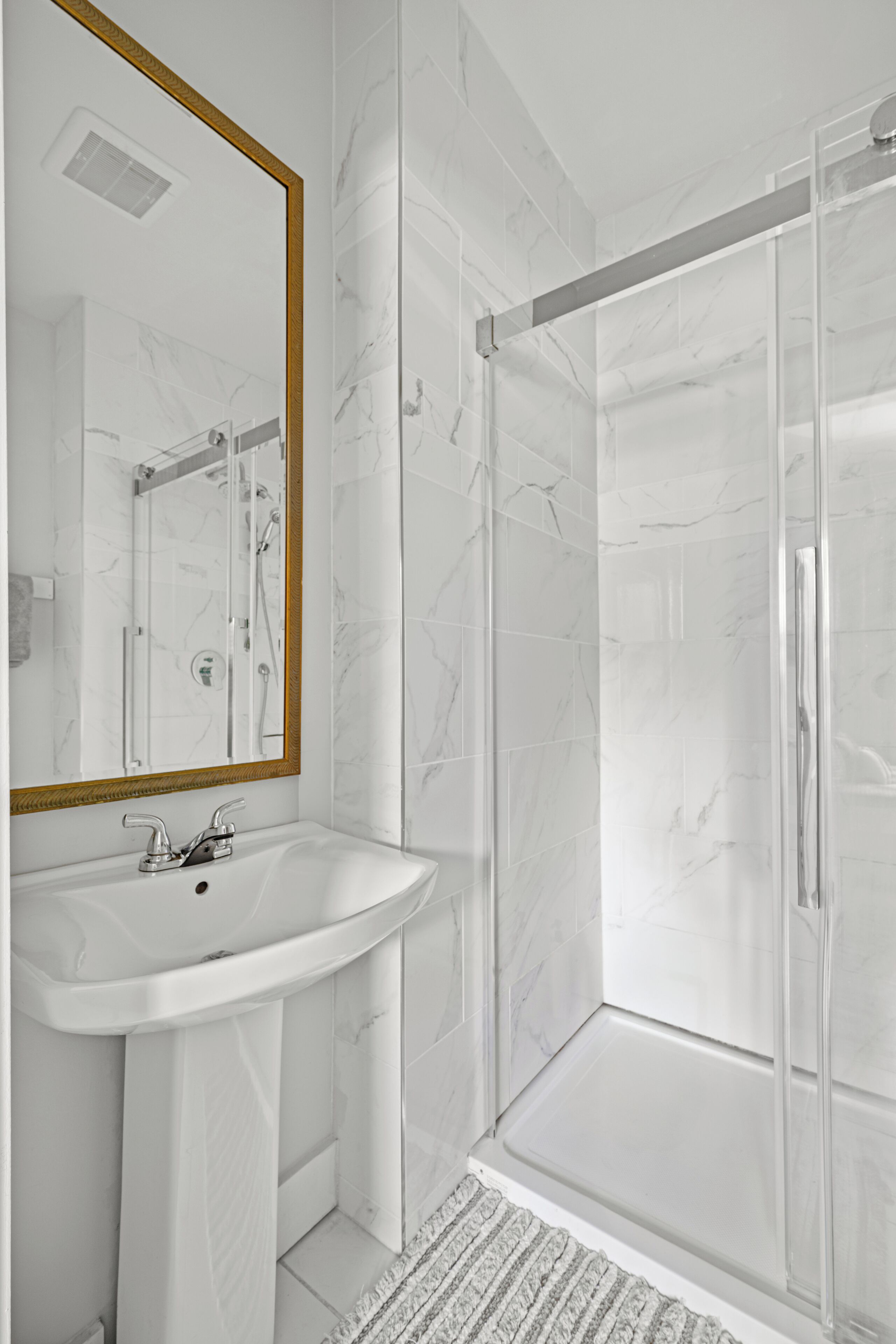 A modern bathroom with a white marble sink, a large mirror, and a glass-enclosed shower area.